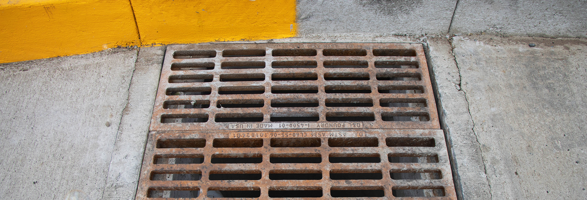 Storm drain with grate. Yellow curb behind and concrete surrounding.
