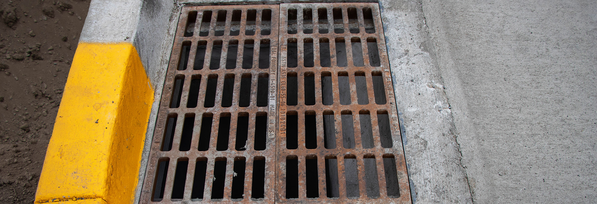 Storm drain with grate. Yellow curb behind and concrete surrounding.