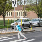 Child crossing a crosswalk on a street with a car waiting.