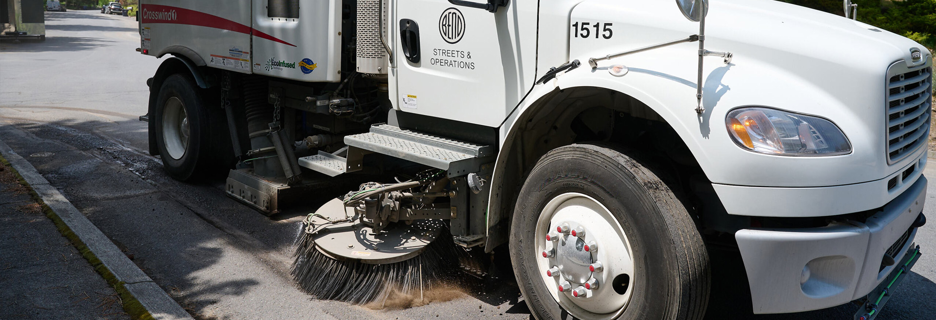 White street sweeper vehicle sweeping a city street.