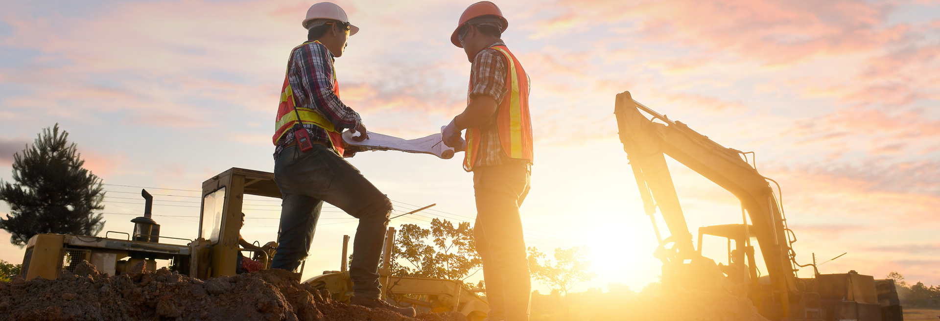 Two construction workers looking at blueprints with a sunset behind them.