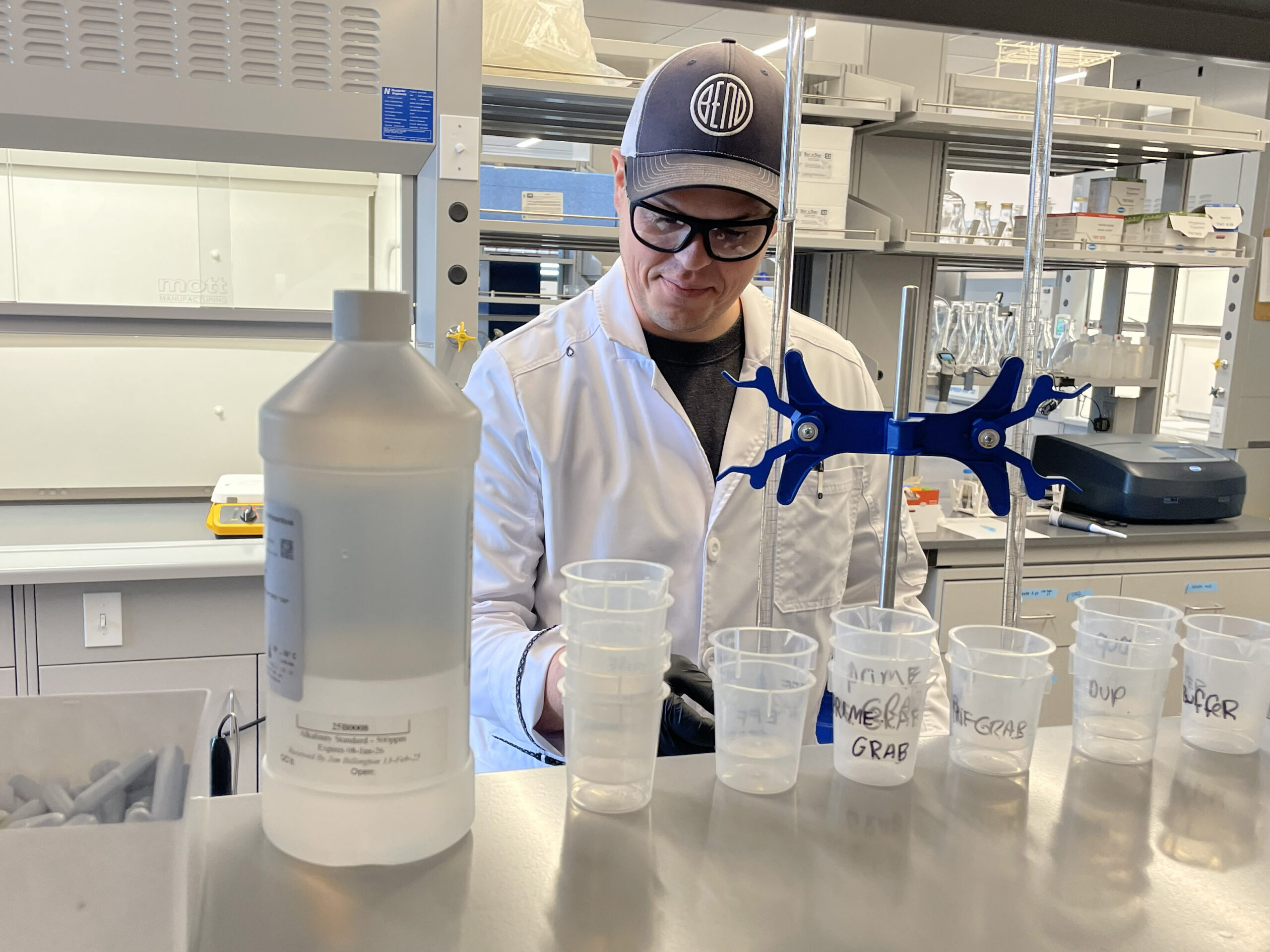 Man in a lab coat wearing a hat uses lab equipment in a scientific laboratory.