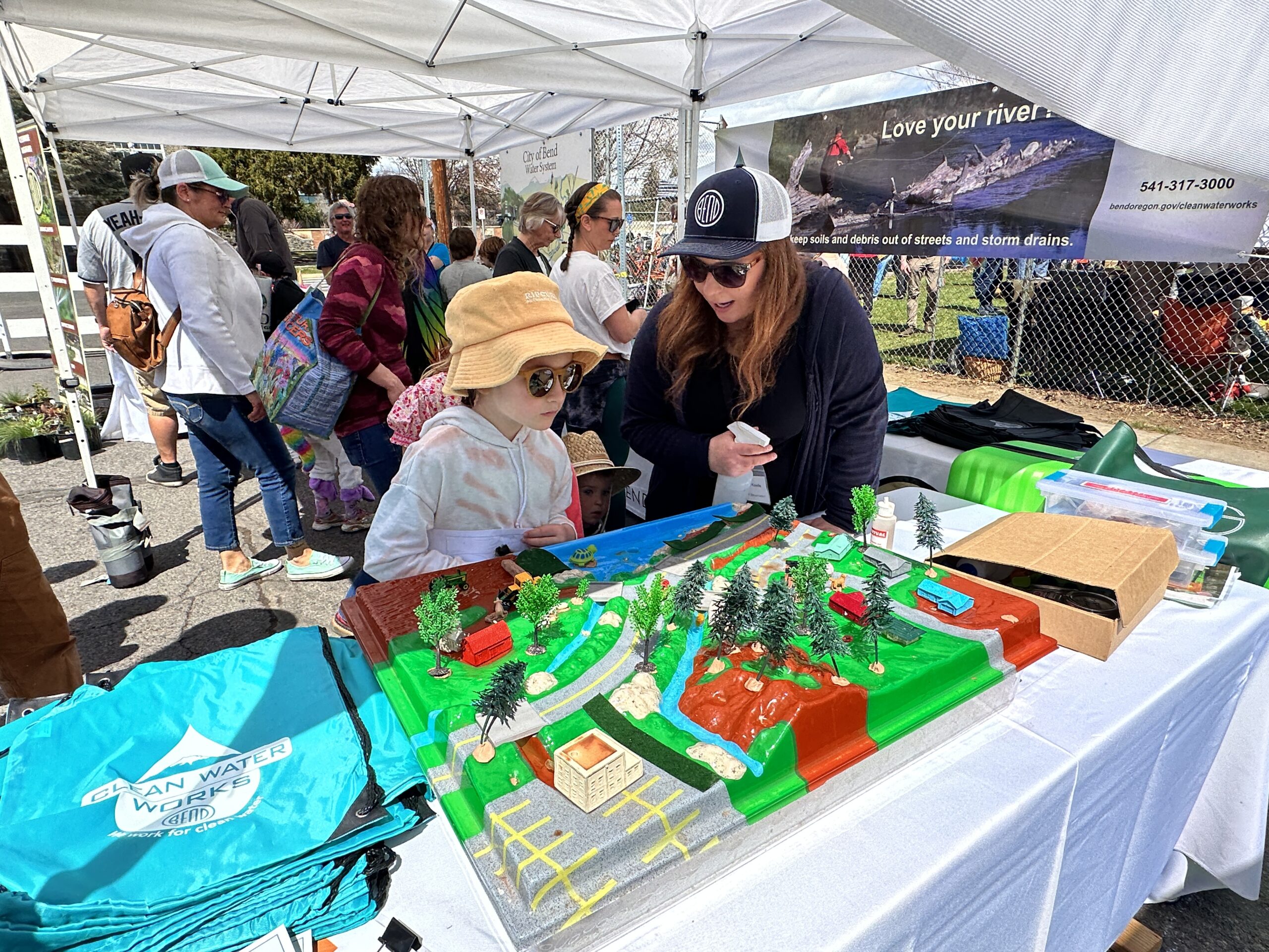 A woman talks to a child inside an event tent while both look at a model urban landscape