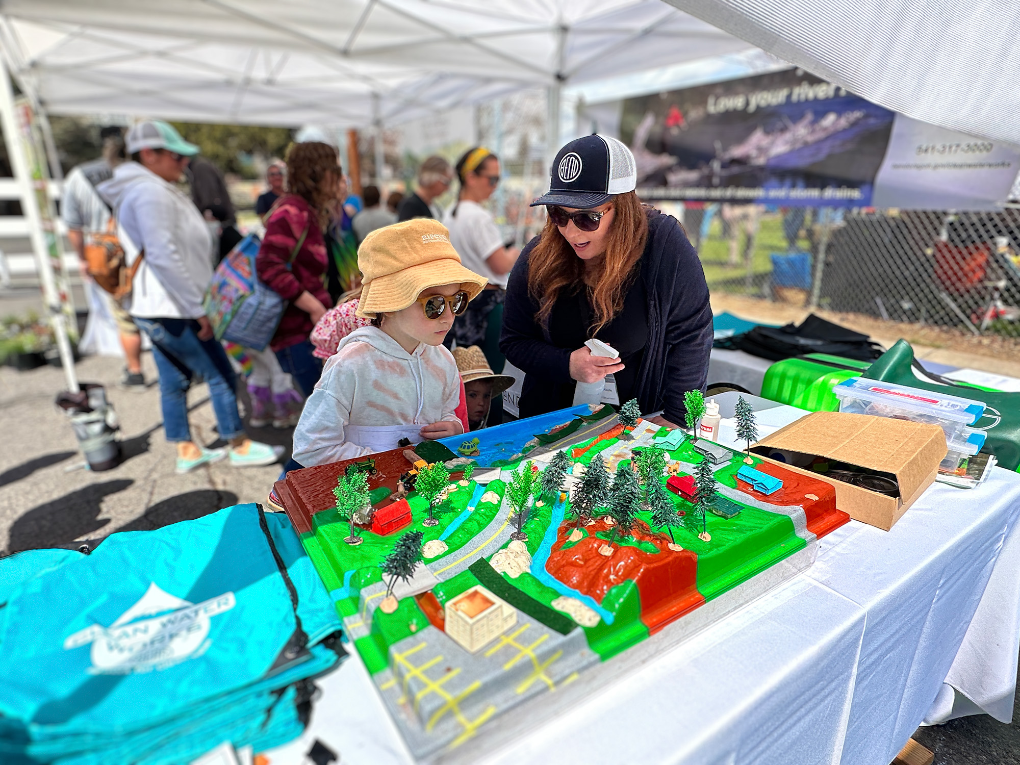 A woman talks to a child inside an event tent while both look at a model urban landscape