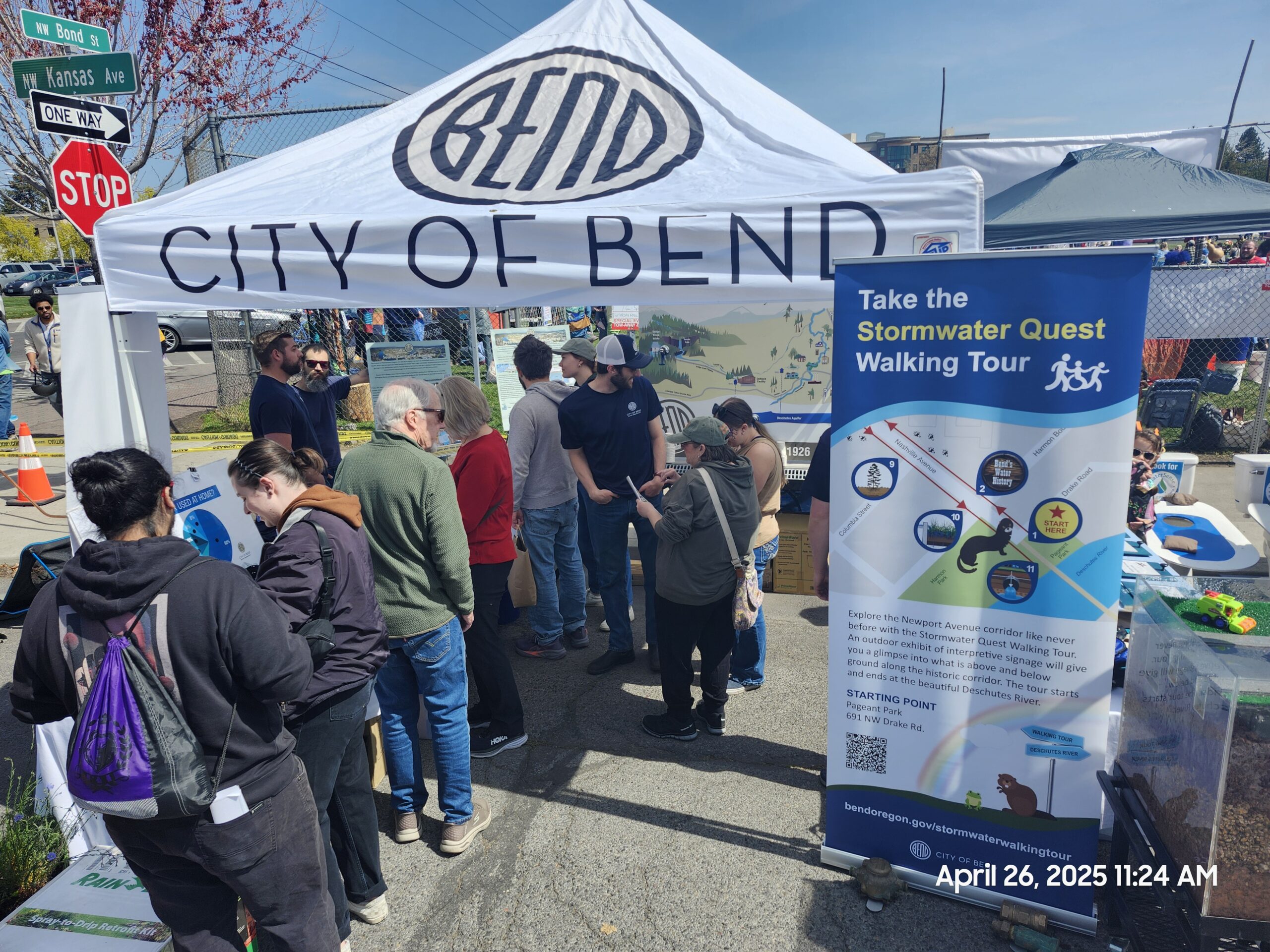 Crowd of people wait to enter City of Bend branded tent at street fair.
