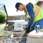 A person works on a water meter box in the ground