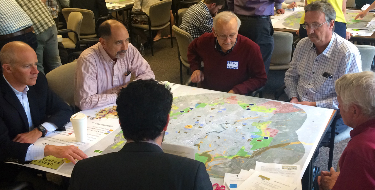 Group of people sitting around a table looking at and discussing a map.