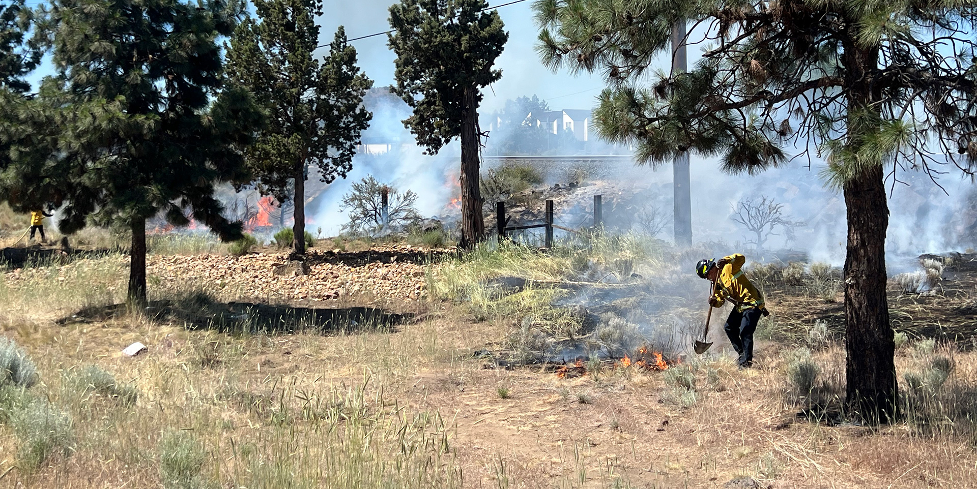 Firefighter working on putting out a small fire in brush, smoke is rising from the fire.