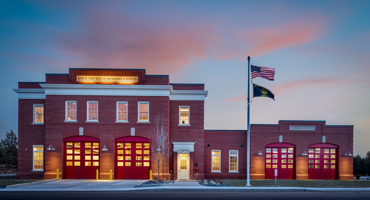 Fire Station at sunset, brick building with flag pole in front.