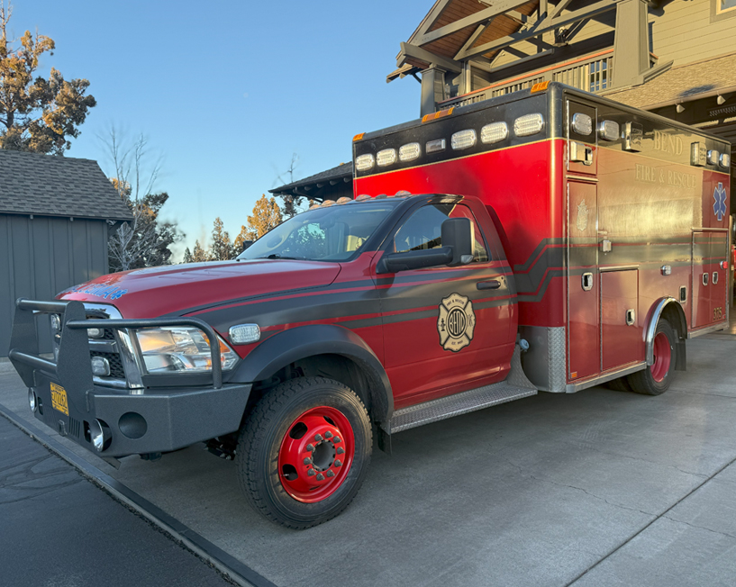 A red and black ambulance sitting in front of a fire station.