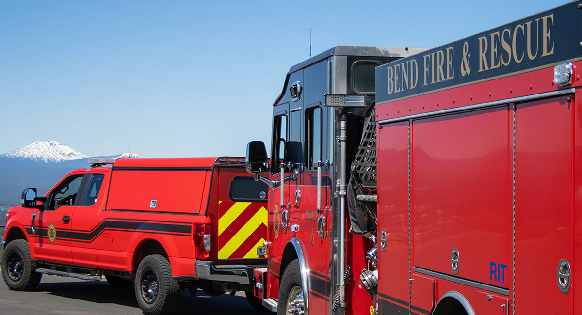 Two red fire engines with a blue sky and snow-capped mountain in the background.