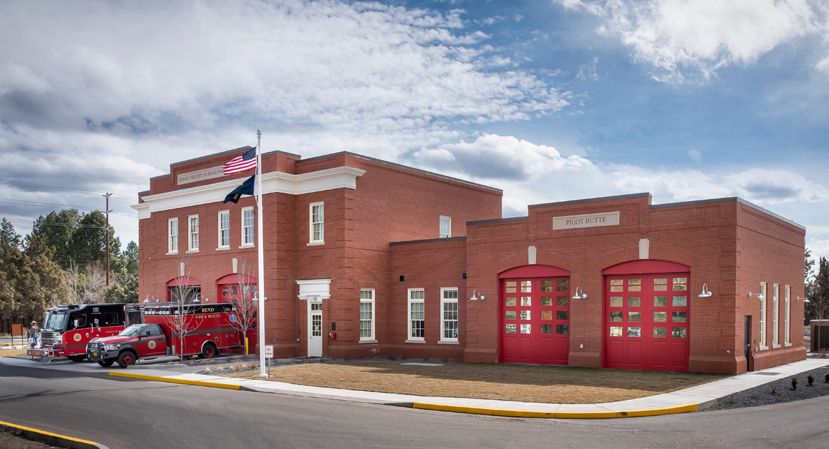 Pilot Butte Fire Station exterior. The building is covered with brick. There are two Fire & Rescue vehicles in front of the building. The