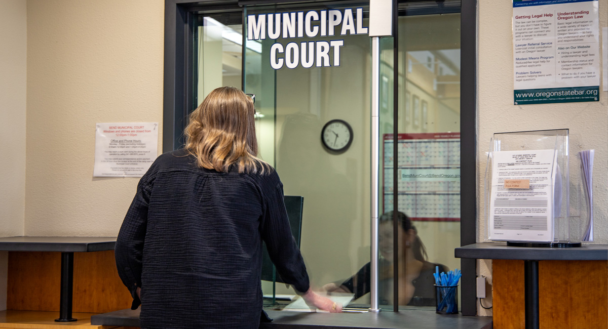 Person handing someone sitting down a piece of paper. The Word 'Municipal Court' are at the top of the picture.