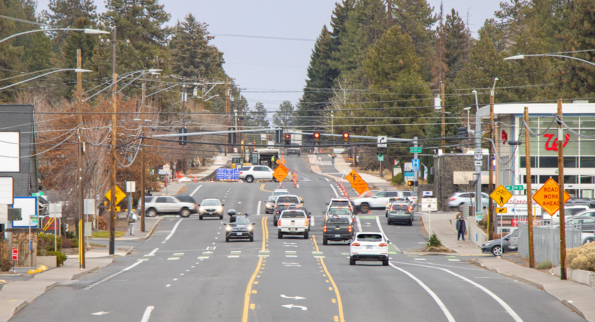Cars traveling on a street near a busy intersection with a stoplight. Road construction is happening in the distance.