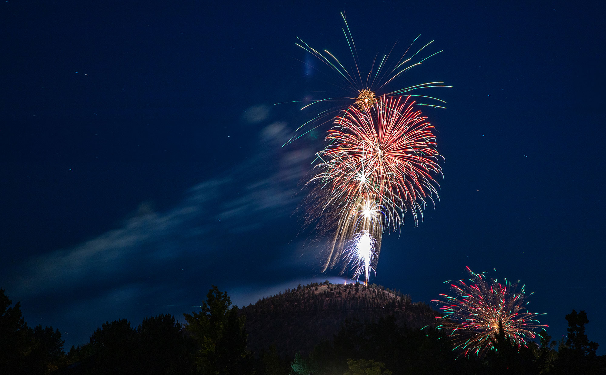 Fireworks being deployed from the top of a hill with the night sky in the background.
