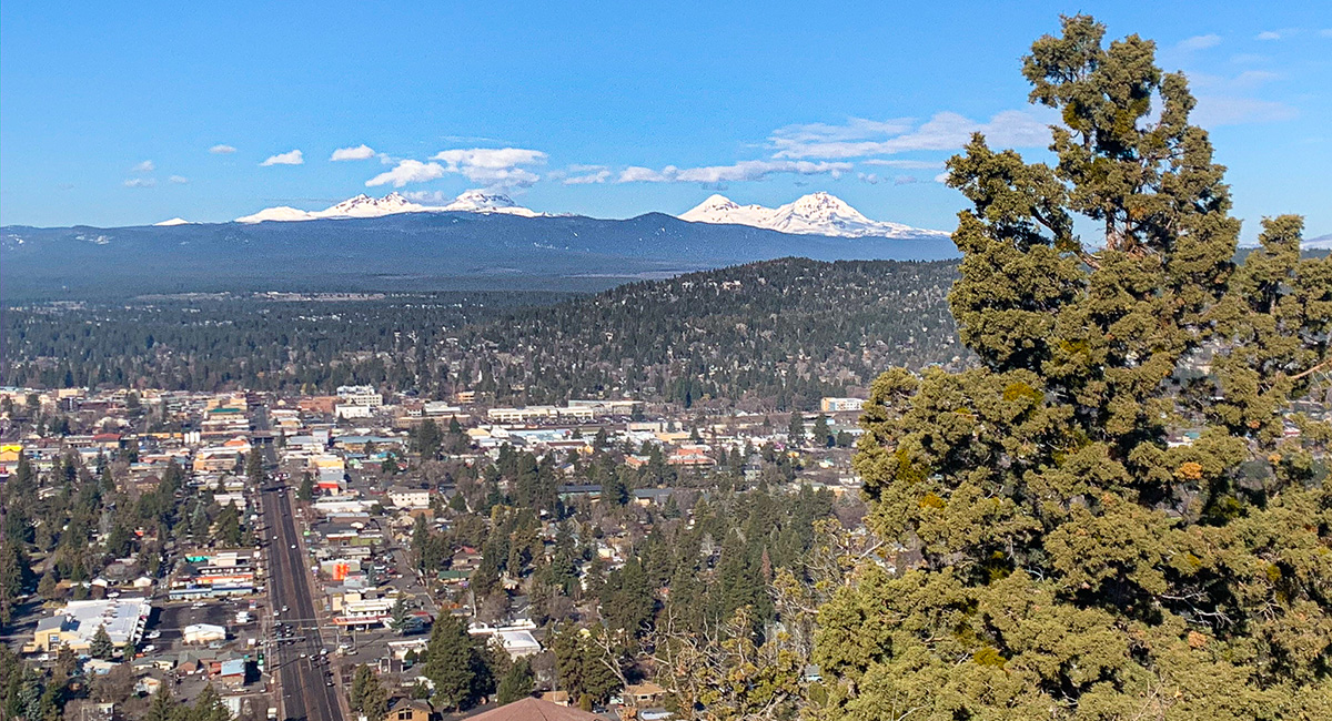 City of Bend image from the top of Pilot Butte. Streets, buildings, and mountains in the background.