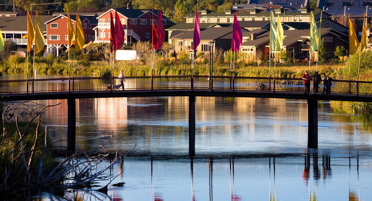 Footbridge over a river with colorful flags attached to it.