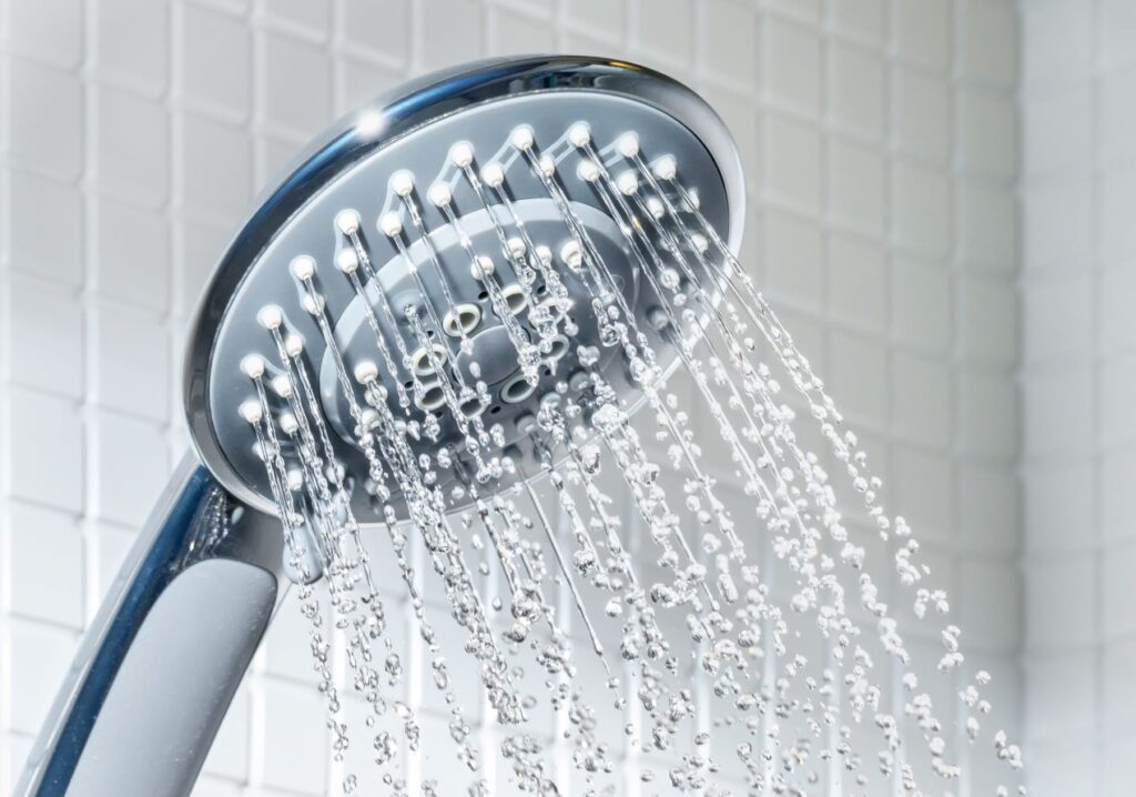 Water coming out of a silver shower head with white tile background