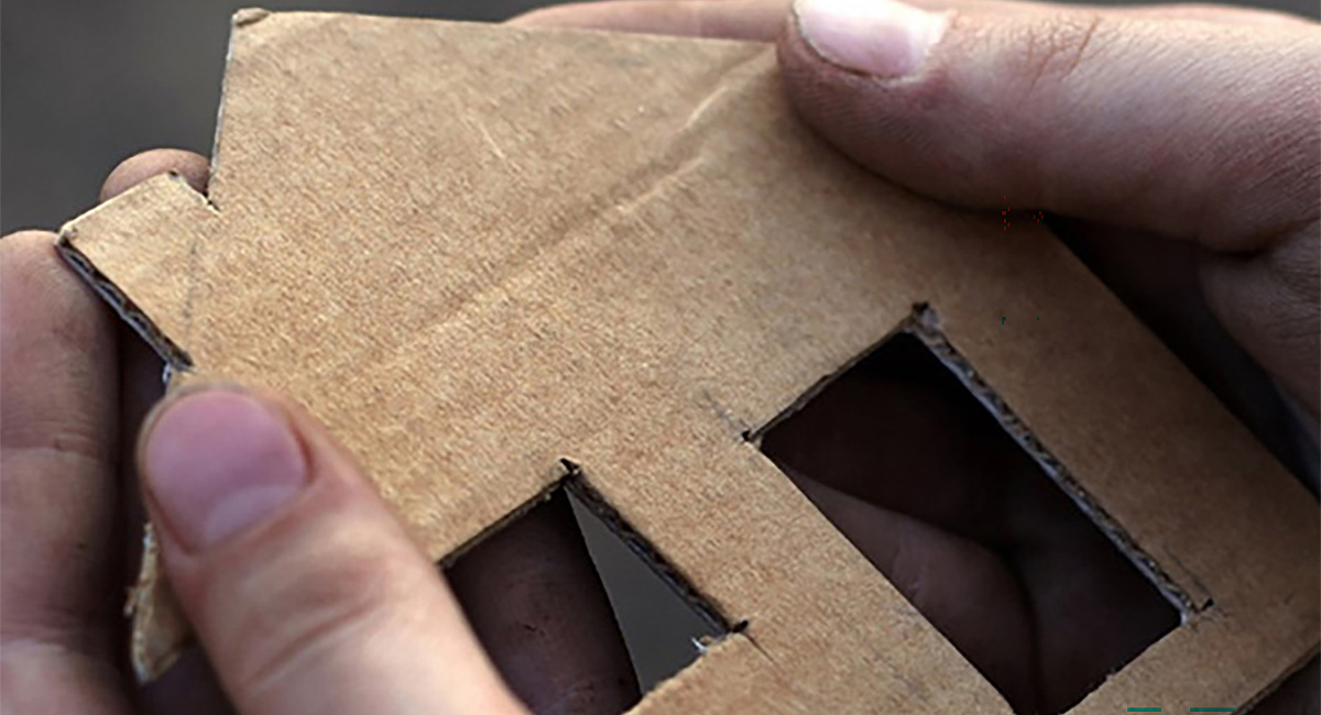 Hands holding a cardboard cutout of a house.