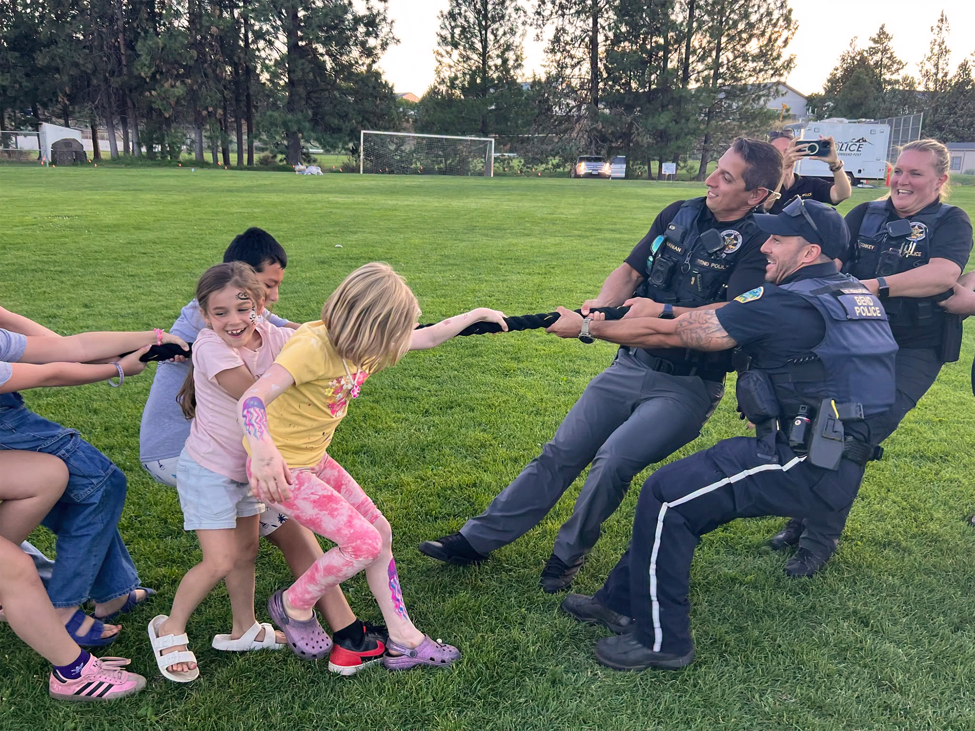 Police officers engaging in a fun game of tug-o-war with children on a grassy field.