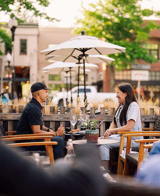 Two people facing each other and talking sitting outside at a restaurant in downtown Bend.