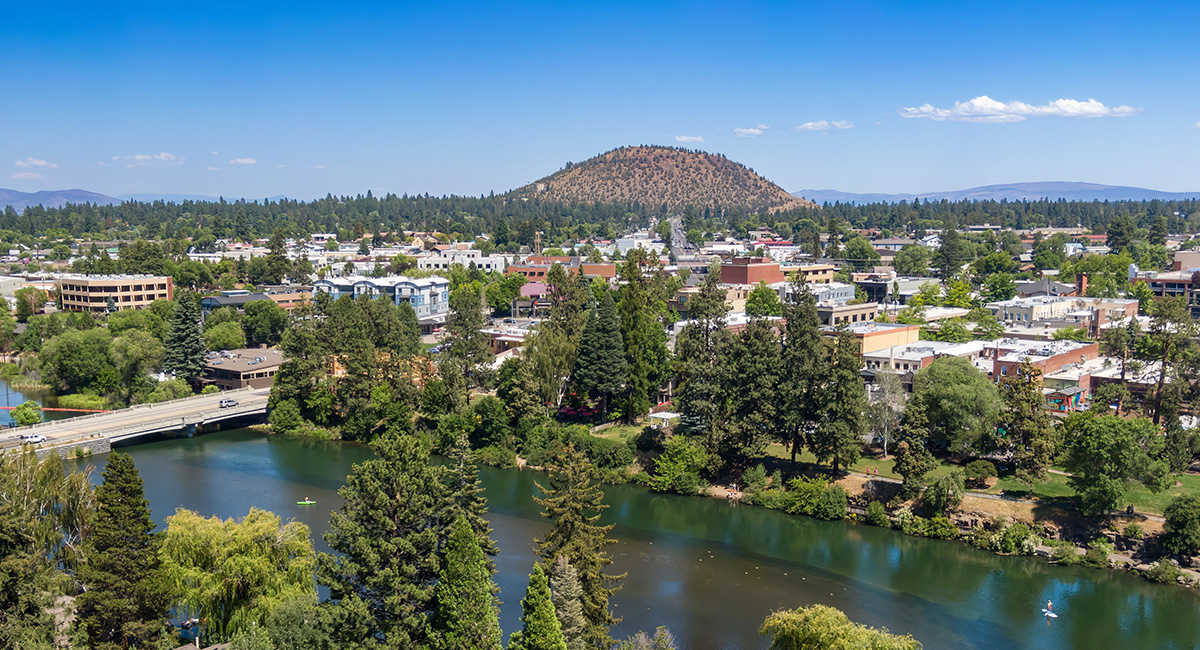 City of Bend looking east with Pilot Butte in the mid-ground. Buildings, roads, and Trees.