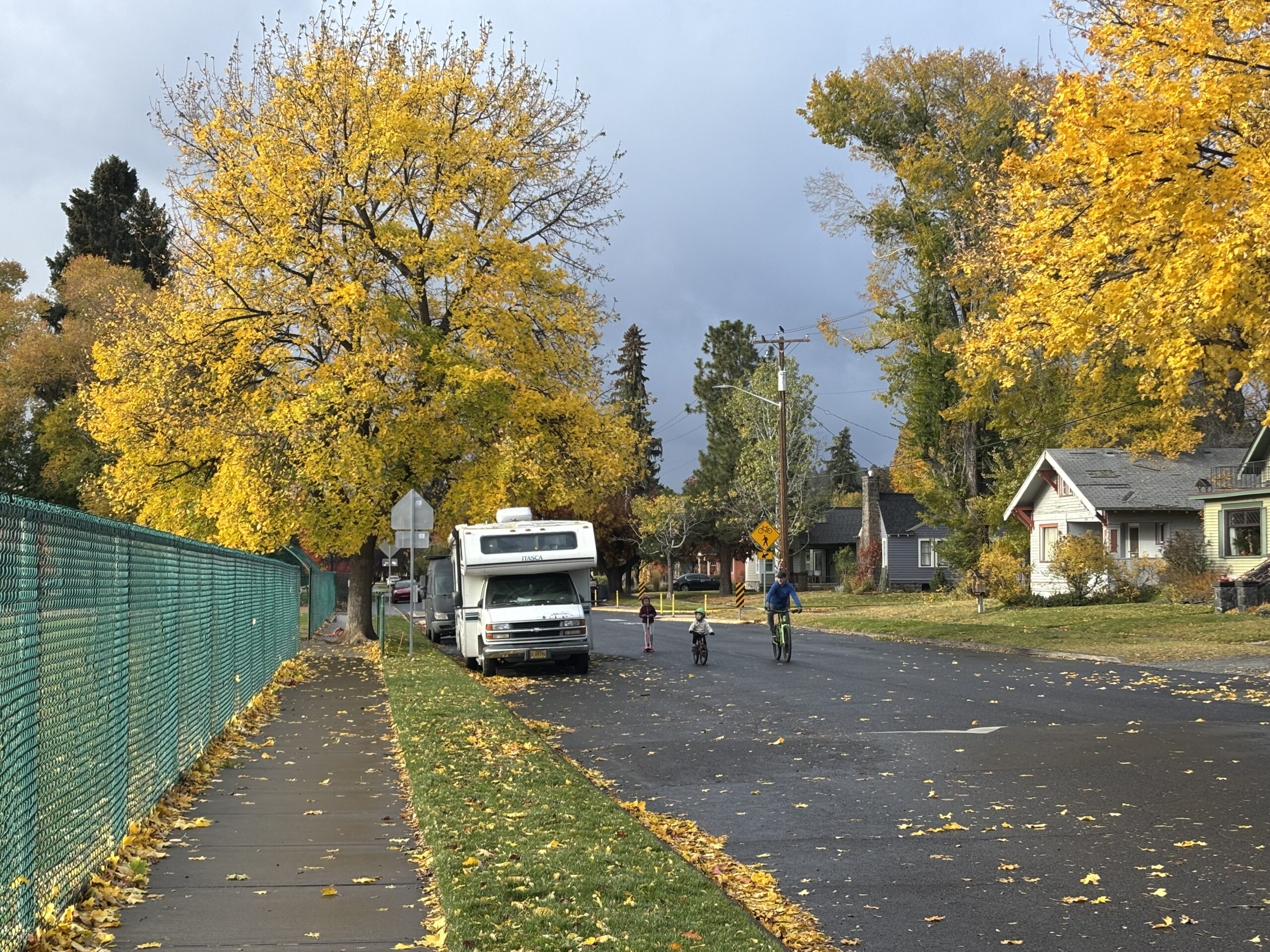 A Family rides bikes down a neighborhood street with a speed bump.