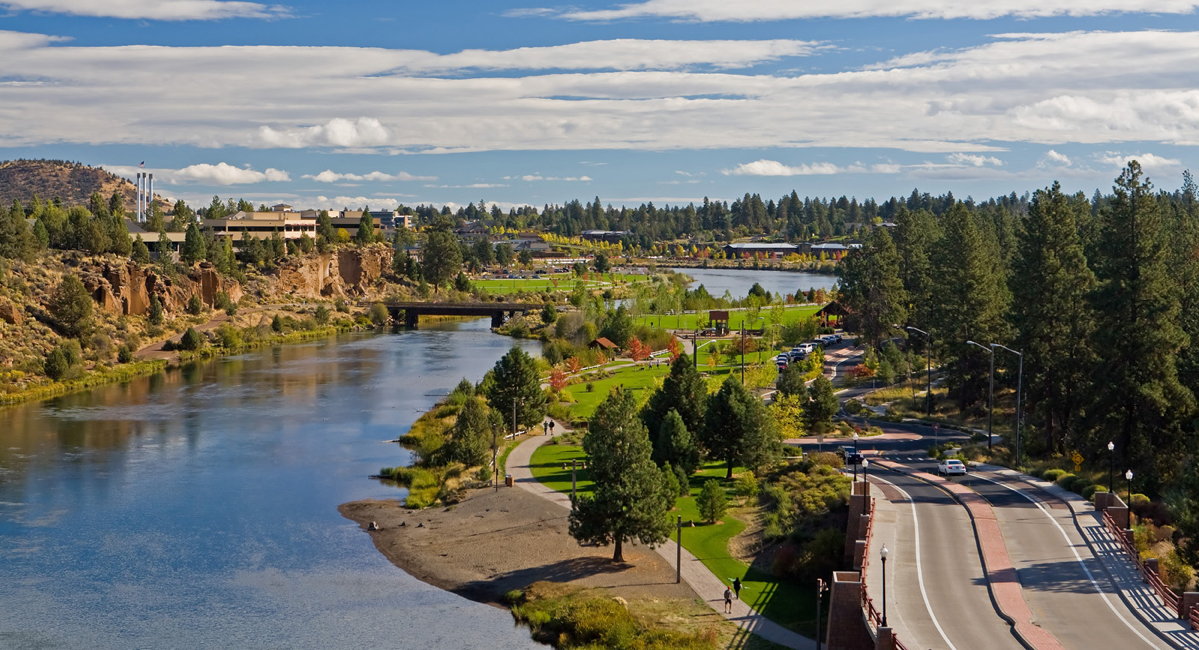 Deschutes River flowing through two parks, bridge in the foreground, partly cloudy skies in the background.