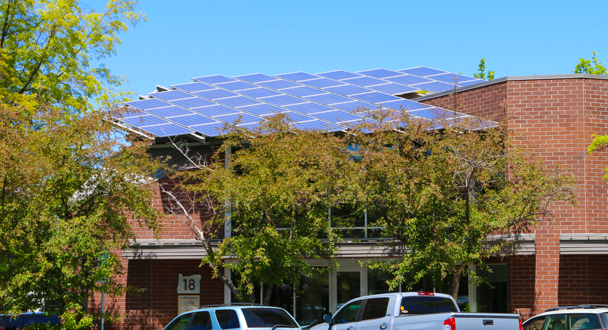 Brick building with leafy trees in front and solar panels on the roof.